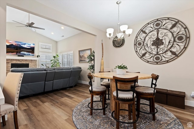 dining room with a fireplace, dark wood-type flooring, ceiling fan with notable chandelier, and vaulted ceiling