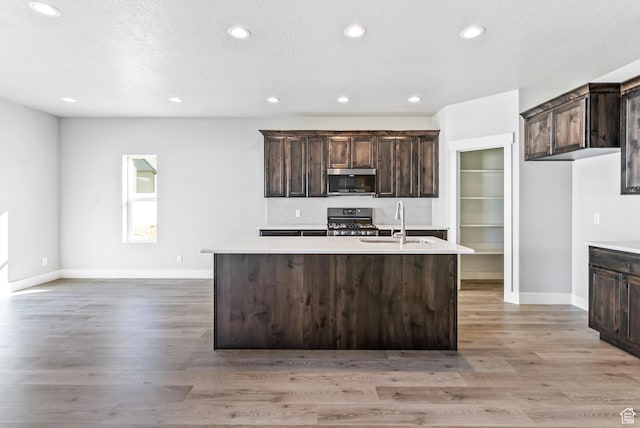 kitchen with an island with sink, gas range, and light wood-type flooring