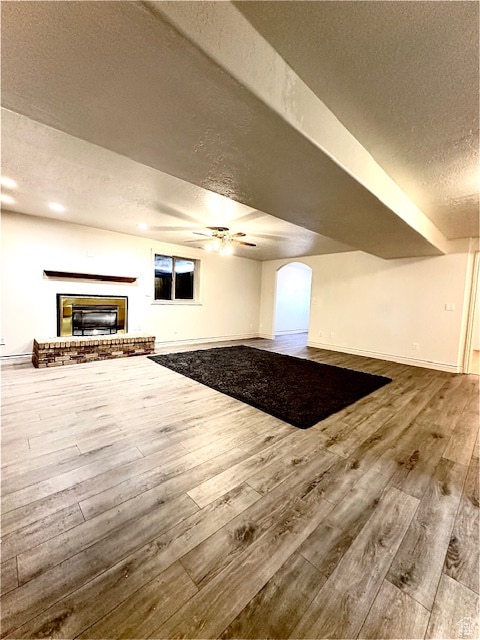 bonus room with a brick fireplace, wood-type flooring, a textured ceiling, and ceiling fan