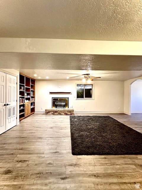 unfurnished living room with a textured ceiling, hardwood / wood-style flooring, a brick fireplace, built in shelves, and ceiling fan