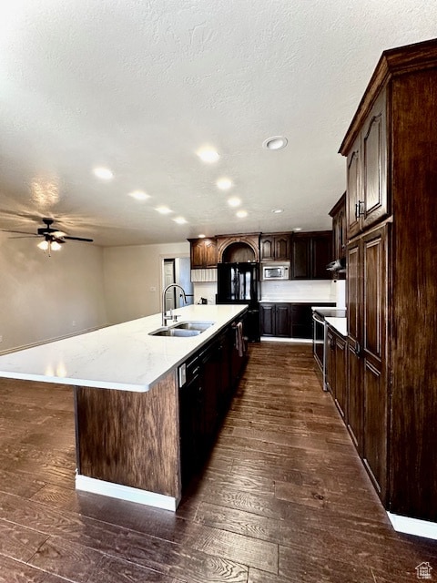 kitchen with black appliances, sink, dark hardwood / wood-style floors, a kitchen island with sink, and dark brown cabinets