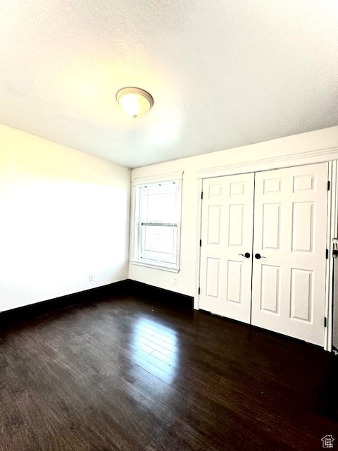 unfurnished bedroom featuring a closet, a textured ceiling, and dark hardwood / wood-style flooring