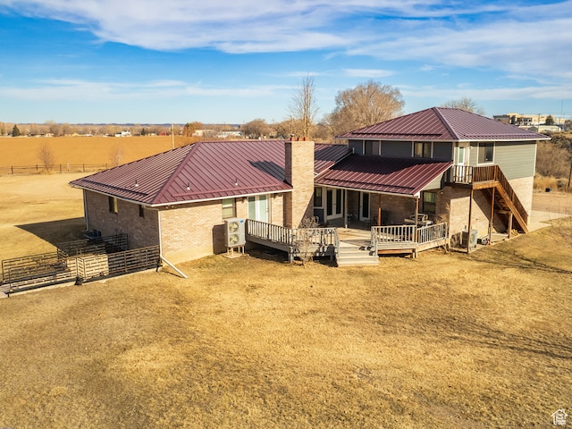 back of property with a wooden deck, a yard, and a rural view
