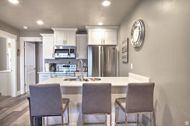 55 W Buttercup Ln Unit 26, Garden City, UT 84028 - kitchen with hardwood / wood-style flooring, white cabinetry, stainless steel appliances, sink, and a kitchen breakfast bar