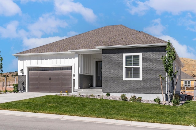 view of front of house featuring a front yard, roof with shingles, concrete driveway, an attached garage, and board and batten siding