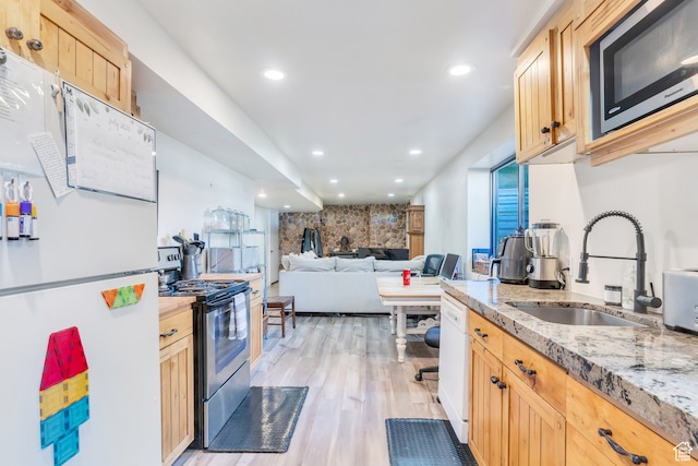 kitchen with light stone countertops, appliances with stainless steel finishes, sink, light wood-type flooring, and light brown cabinetry