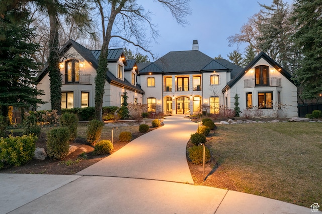 view of front facade with concrete driveway, french doors, a chimney, a balcony, and a standing seam roof