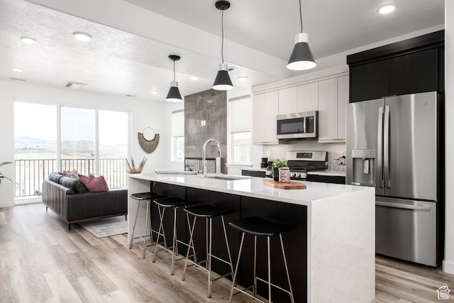 4119 S Winder Ward Dr E Unit 3-106, Millcreek, UT 84124 - kitchen with appliances with stainless steel finishes, a kitchen bar, a sink, light wood-style floors, and an island with sink