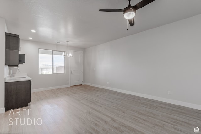 unfurnished living room with sink, light hardwood / wood-style flooring, and ceiling fan with notable chandelier