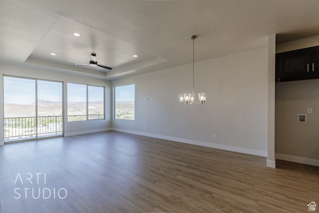 spare room with a textured ceiling, a tray ceiling, wood-type flooring, ceiling fan with notable chandelier, and a mountain view