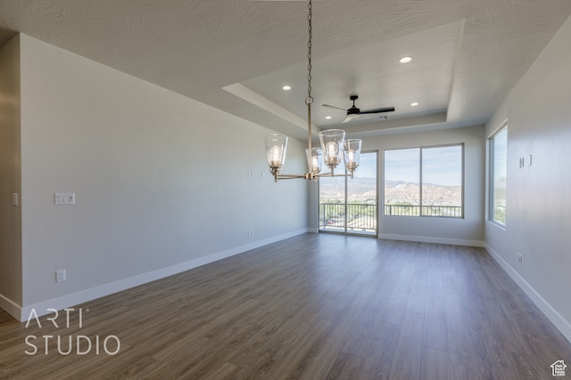 unfurnished dining area with dark wood-type flooring, a textured ceiling, a tray ceiling, and ceiling fan with notable chandelier