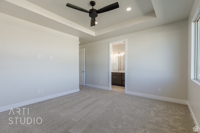 unfurnished bedroom featuring ensuite bathroom, light carpet, a tray ceiling, and ceiling fan