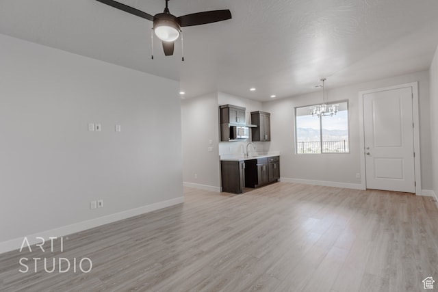unfurnished living room with light hardwood / wood-style flooring, a textured ceiling, sink, and ceiling fan with notable chandelier