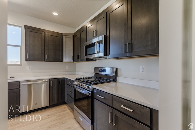 kitchen featuring a textured ceiling, stainless steel appliances, dark brown cabinets, and light wood-type flooring