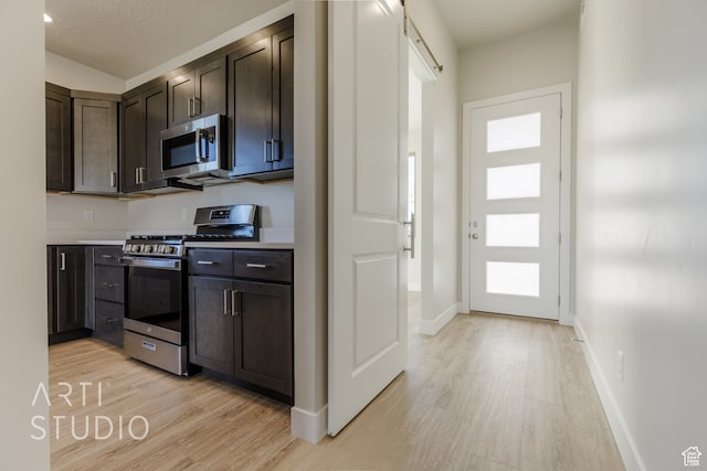 kitchen featuring appliances with stainless steel finishes, a textured ceiling, a barn door, light hardwood / wood-style flooring, and dark brown cabinetry