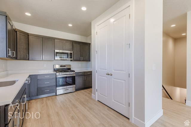 kitchen with appliances with stainless steel finishes, dark brown cabinets, and light hardwood / wood-style floors