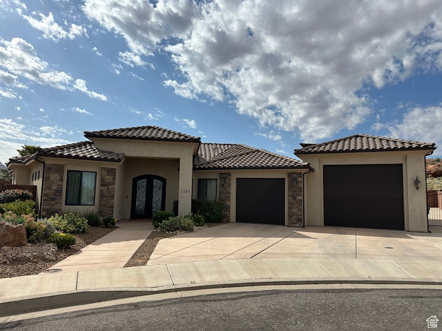 mediterranean / spanish house featuring a tile roof, stucco siding, driveway, stone siding, and an attached garage