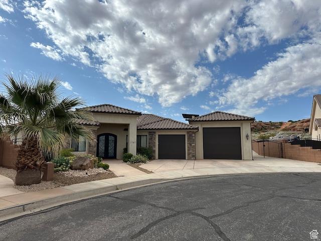 mediterranean / spanish-style home featuring a tile roof, concrete driveway, stucco siding, an attached garage, and a gate