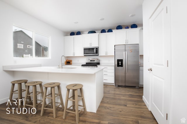kitchen with a breakfast bar area, stainless steel appliances, dark wood-type flooring, white cabinets, and sink