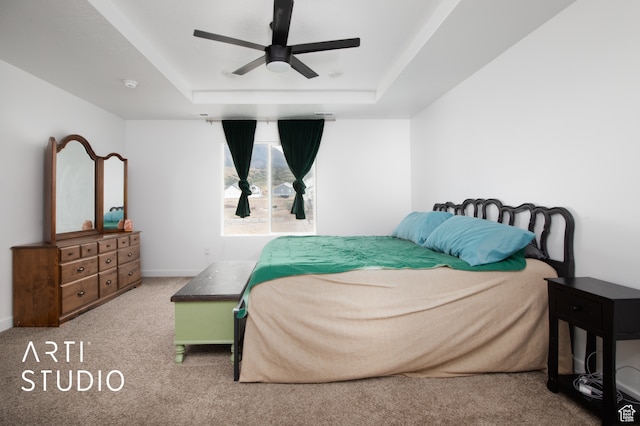 carpeted bedroom with ceiling fan and a raised ceiling
