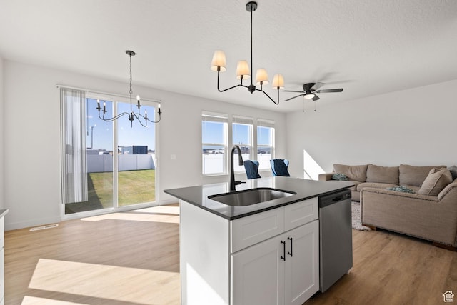 kitchen featuring dishwasher, dark countertops, a sink, light wood-style floors, and an inviting chandelier