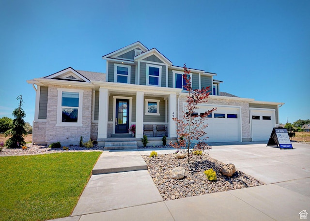 craftsman house featuring driveway, board and batten siding, stone siding, a front yard, and covered porch