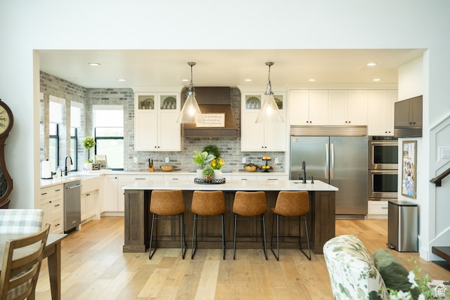kitchen featuring a kitchen island with sink, light wood-style floors, light countertops, white cabinets, and stainless steel appliances
