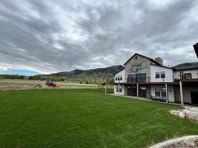 back of house with a lawn, a mountain view, a chimney, and stone siding
