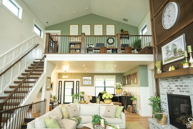 living area with visible vents, a fireplace, wood finished floors, stairway, and high vaulted ceiling