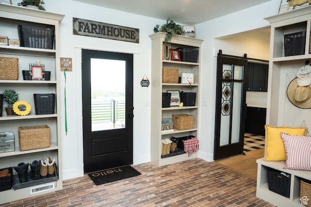 mudroom with visible vents, a barn door, and brick floor