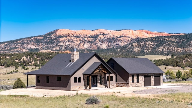 view of front of property featuring stone siding, a chimney, a garage, dirt driveway, and a mountain view