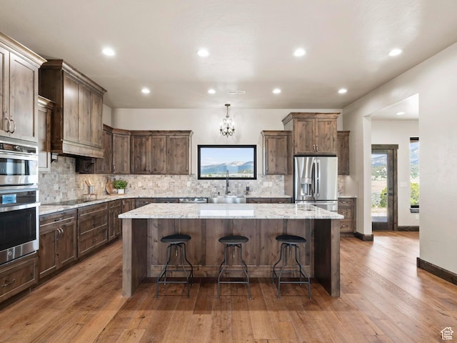 kitchen featuring decorative backsplash, dark brown cabinets, a kitchen island, appliances with stainless steel finishes, and a sink