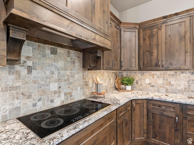 kitchen with black electric cooktop, exhaust hood, light stone counters, and tasteful backsplash