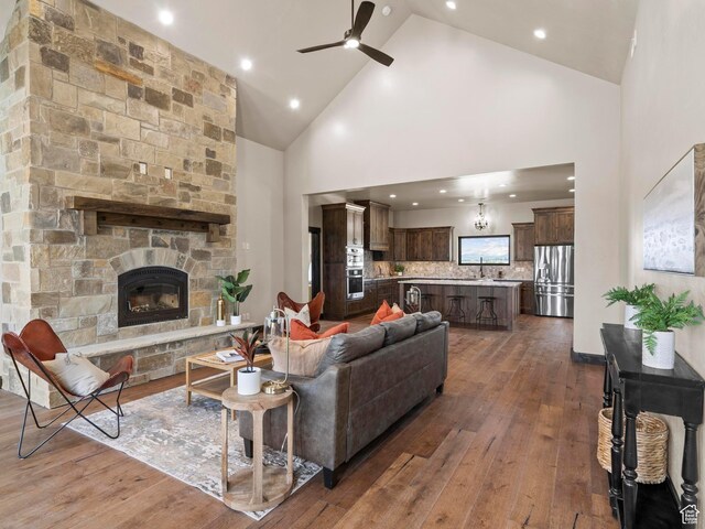 living room featuring high vaulted ceiling, wood-type flooring, a stone fireplace, ceiling fan, and recessed lighting