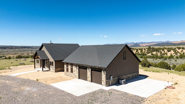 view of front of house with stone siding, concrete driveway, central AC unit, a garage, and a mountain view