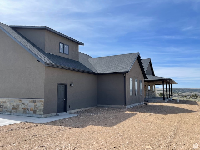 view of property exterior with stucco siding, stone siding, and roof with shingles