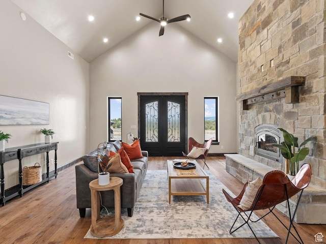 living room featuring high vaulted ceiling, visible vents, a ceiling fan, a stone fireplace, and wood finished floors