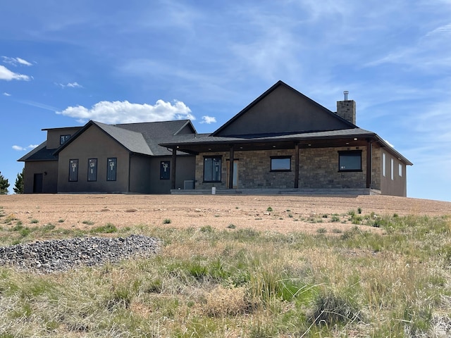 rear view of property featuring stone siding, stucco siding, and a chimney