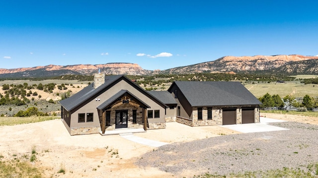 modern farmhouse featuring stone siding, an attached garage, driveway, a mountain view, and french doors