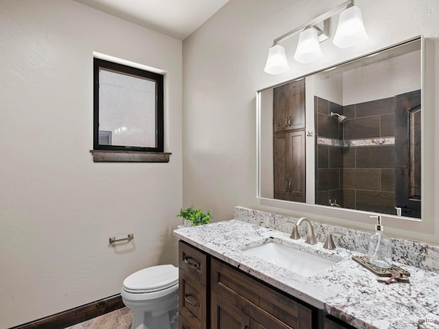 bathroom with toilet, vanity, baseboards, and tiled shower