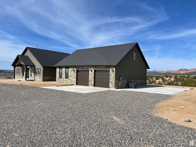 view of front of house with stone siding, a garage, concrete driveway, and a mountain view
