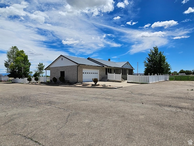 view of front of property featuring brick siding, metal roof, fence, a garage, and driveway