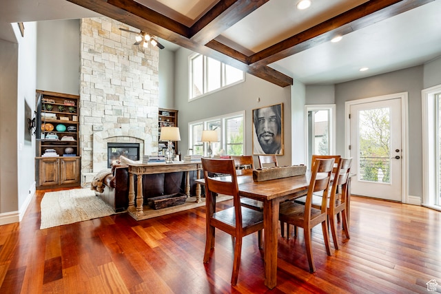 dining room featuring wood-type flooring, ceiling fan, beam ceiling, and a fireplace