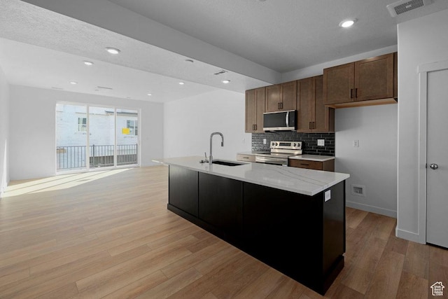 4126 S Winder Ward Dr Unit 2-123, Millcreek, UT 84124 - kitchen with appliances with stainless steel finishes, a sink, light wood finished floors, tasteful backsplash, and a center island with sink