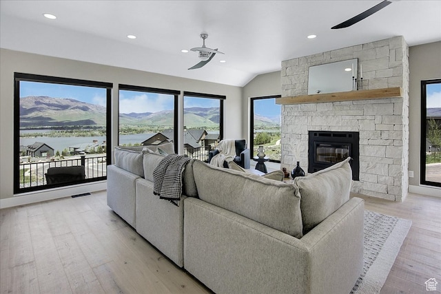 living room with ceiling fan, a stone fireplace, a mountain view, and light hardwood / wood-style flooring