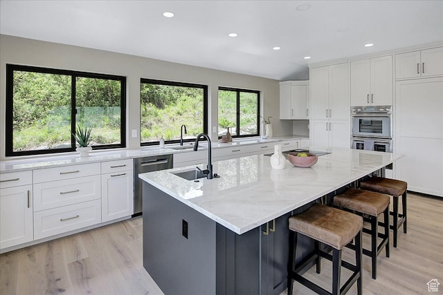 kitchen featuring light hardwood / wood-style floors, white cabinetry, a kitchen breakfast bar, stainless steel appliances, and a kitchen island with sink