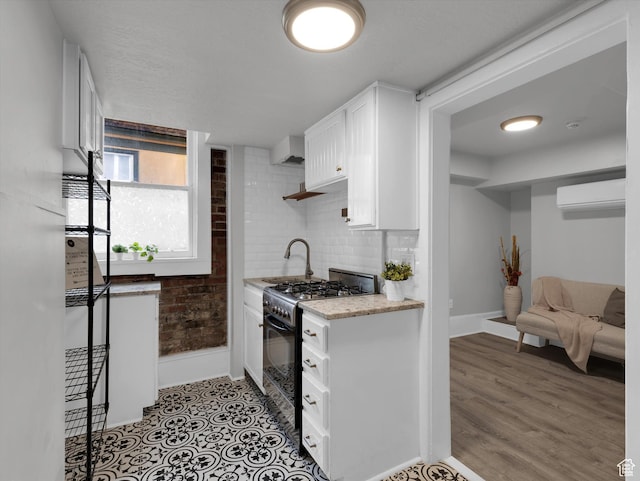 86 B St E Unit 10, Salt Lake City, UT 84103 - kitchen with light wood-type flooring, gas range oven, sink, an AC wall unit, and white cabinetry