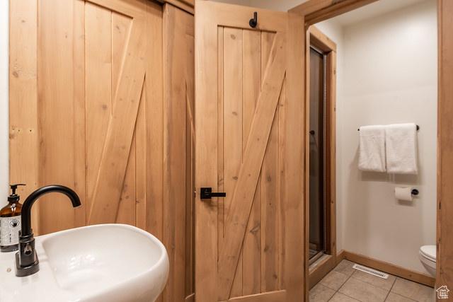 3009 E Black Forest Rd, Sundance, UT 84604 - bathroom with wood walls, a shower with shower door, sink, tile patterned flooring, and toilet