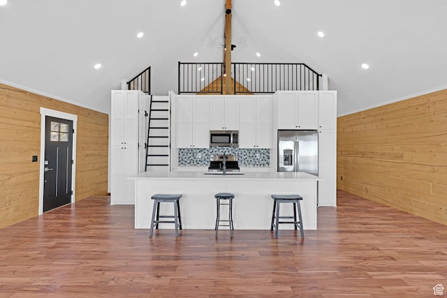999 Cisco Run, Garden City, UT 84028 - kitchen featuring appliances with stainless steel finishes, wood walls, an island with sink, white cabinetry, and a breakfast bar