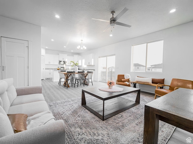 living room with recessed lighting, light wood finished floors, a textured ceiling, and ceiling fan with notable chandelier